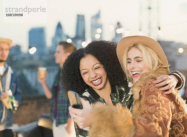 Lachende junge Frauen nehmen Selfie auf Dachparty