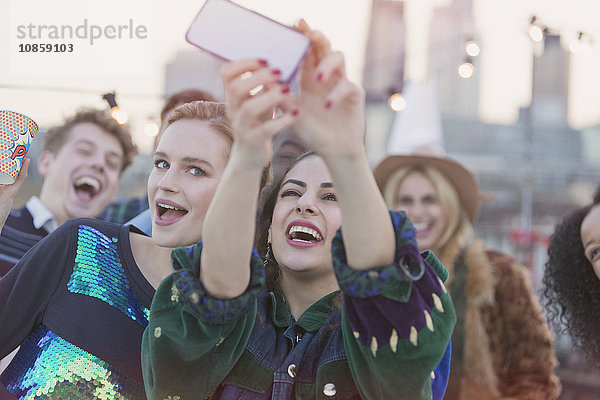 Junge Frauen lachen und nehmen Selfie auf der Dachparty mit.