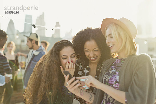 Junge Frauen beim Lachen und SMSen mit dem Handy auf der Dachparty