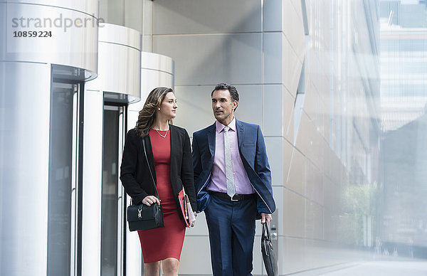 Corporate Geschäftsmann und Geschäftsfrau zu Fuß und sprechen außerhalb des Gebäudes