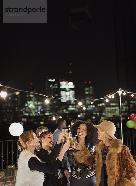 Junge Frauen toasten Cocktails auf der nächtlichen Dachparty
