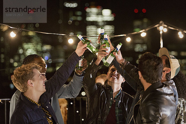 Junge Männer toasten Bierflaschen auf der Dachparty