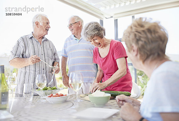 Seniorenpaare bereiten das Mittagessen auf der Terrasse zu.
