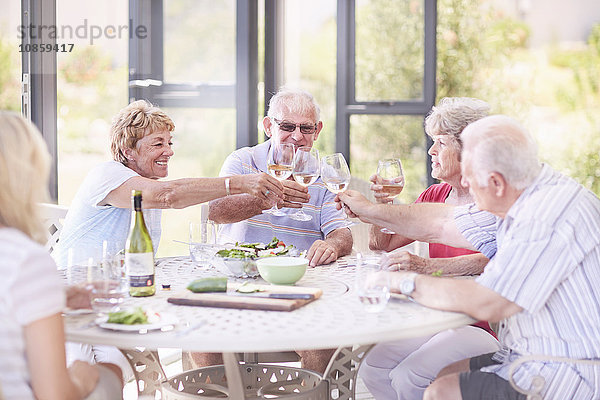 Ältere Erwachsene rösten Weingläser beim Mittagessen auf der Terrasse.