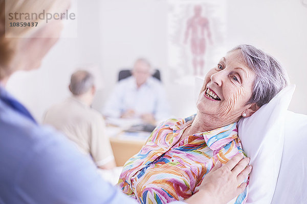 Ärztin tröstet lächelnde Seniorin bei der Untersuchung