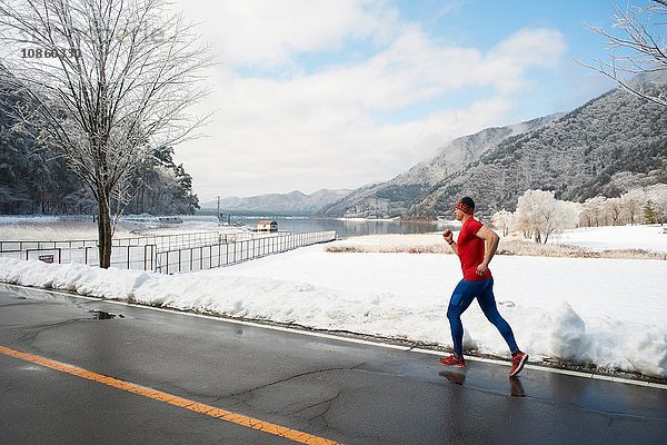 Männlicher Läufer  der im Winter entlang der Straße läuft  Kawaguchiko-See  Berg Fuji  Japan