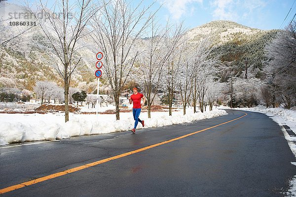 Männlicher Läufer  der im Winter auf der Straße läuft  Kawaguchiko-See  Berg Fuji  Japan