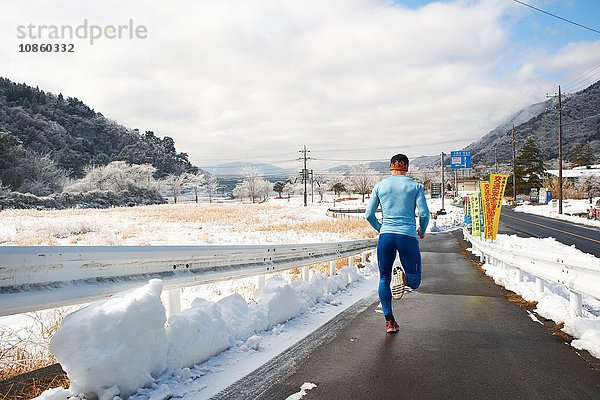 Rückansicht eines reifen männlichen Läufers  der im Winter auf der Straße läuft  Kawaguchiko-See  Berg Fuji  Japan