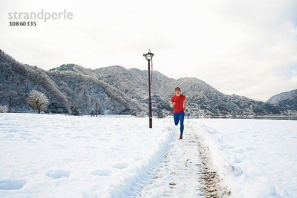 Männlicher Läufer läuft auf schneebedeckten Wegen  Kawaguchiko-See  Berg Fuji  Japan