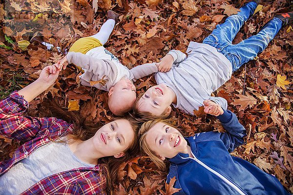 Vier Geschwister auf Herbstblättern liegend