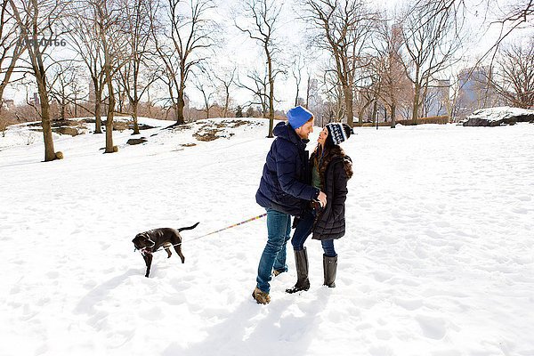 Romantisches junges Paar steht zusammen mit Hund im Schnee  Central Park  New York  USA