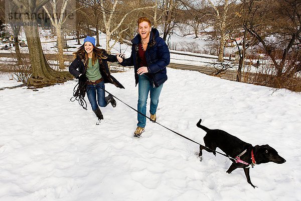Junges Paar rennt mit Hund im verschneiten Central Park  New York  USA