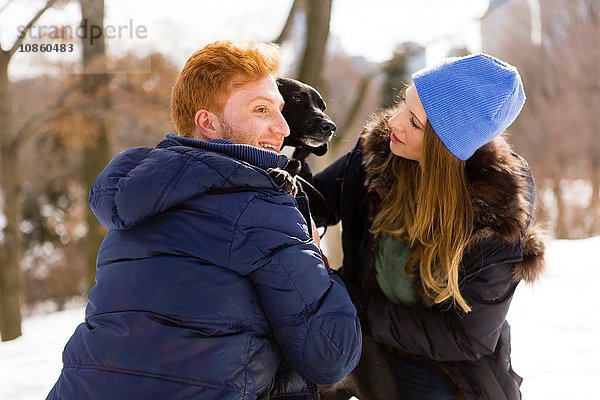 Junges Paar streichelt Hund im verschneiten Central Park  New York  USA