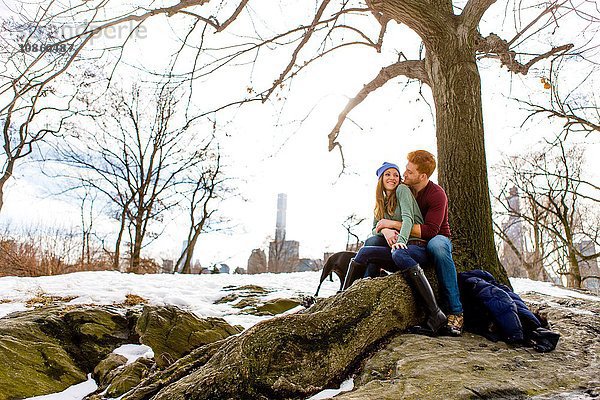 Romantisches junges Paar sitzt mit Hund im verschneiten Central Park  New York  USA