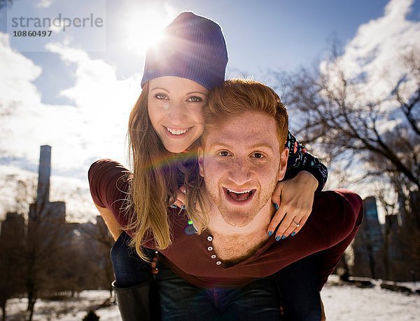 Porträt eines jungen Mannes  der seiner Freundin im verschneiten Central Park ein Huckepack gibt  New York  USA