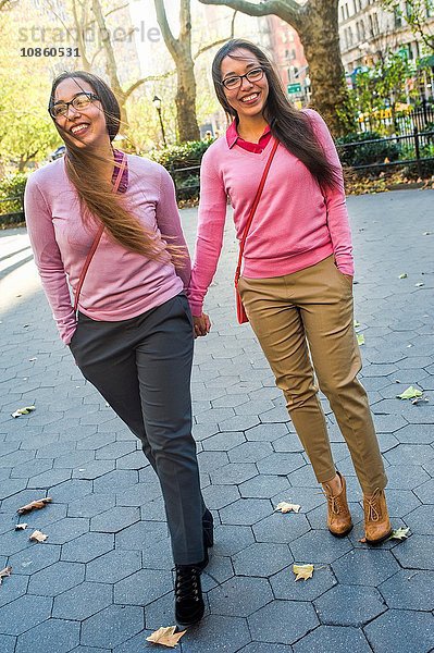 Zwillingsschwestern halten sich an den Händen und gehen auf der Straße