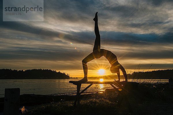 Frau praktiziert Yoga am See bei Sonnenuntergang