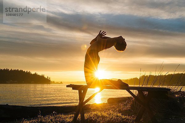 Frau praktiziert Yoga am See bei Sonnenuntergang