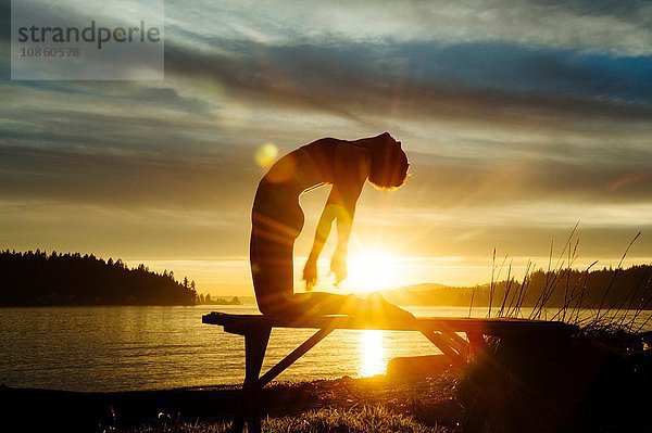 Frau praktiziert Yoga am See bei Sonnenuntergang