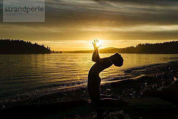 Frau praktiziert Yoga am See bei Sonnenuntergang