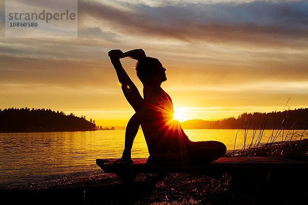 Frau praktiziert Yoga am See bei Sonnenuntergang