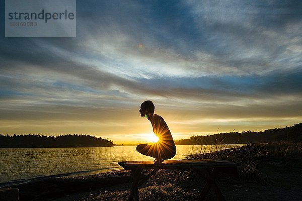 Frau praktiziert Yoga am See bei Sonnenuntergang