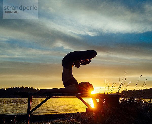 Frau praktiziert Yoga am See bei Sonnenuntergang