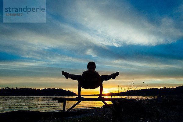 Frau praktiziert Yoga am See bei Sonnenuntergang