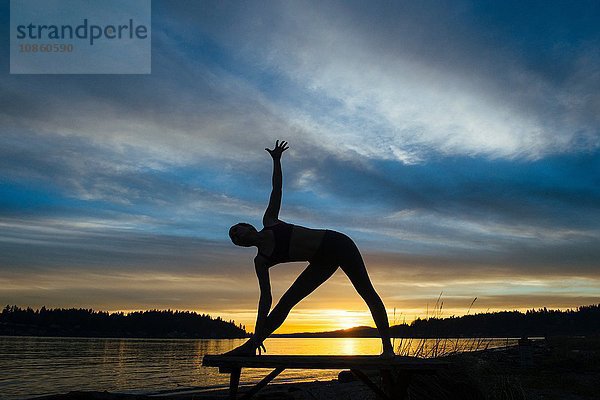 Frau praktiziert Yoga am See bei Sonnenuntergang