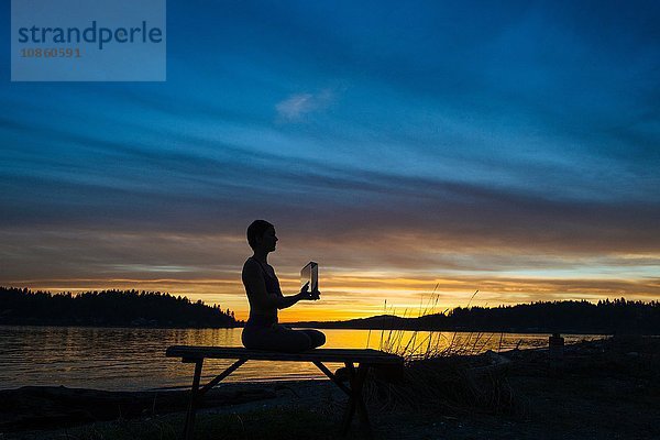 Frau praktiziert Yoga am See bei Sonnenuntergang