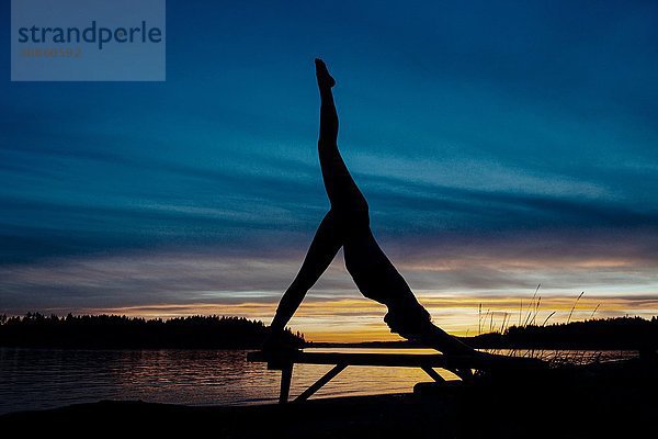 Frau praktiziert Yoga am See bei Sonnenuntergang