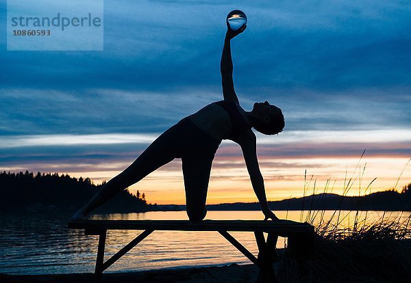 Frau praktiziert Yoga am See bei Sonnenuntergang