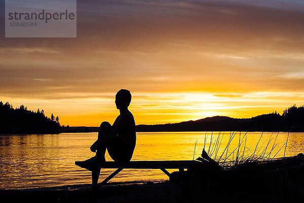 Frau praktiziert Yoga am See bei Sonnenuntergang