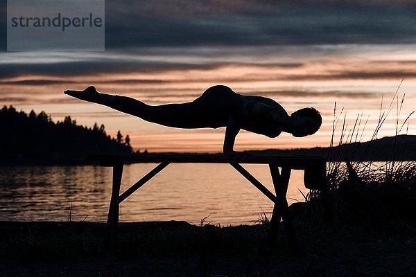 Frau praktiziert Yoga am See bei Sonnenuntergang