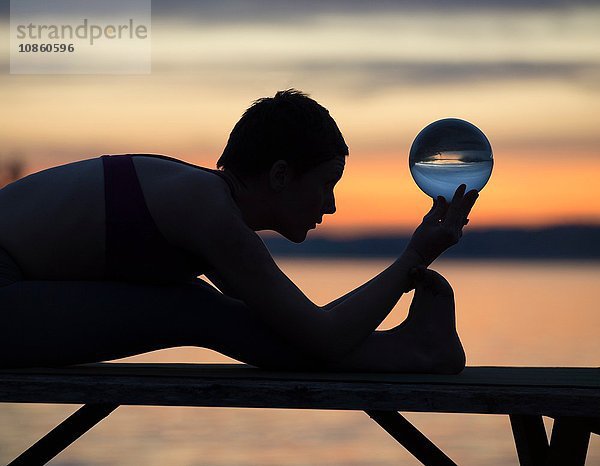 Frau praktiziert Yoga am See bei Sonnenuntergang