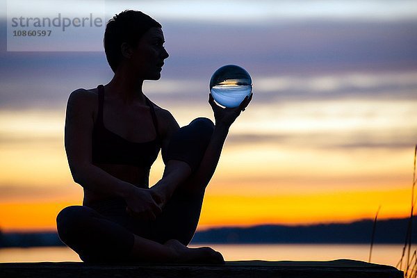 Frau praktiziert Yoga am See bei Sonnenuntergang