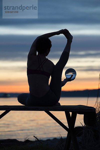 Frau praktiziert Yoga am See bei Sonnenuntergang