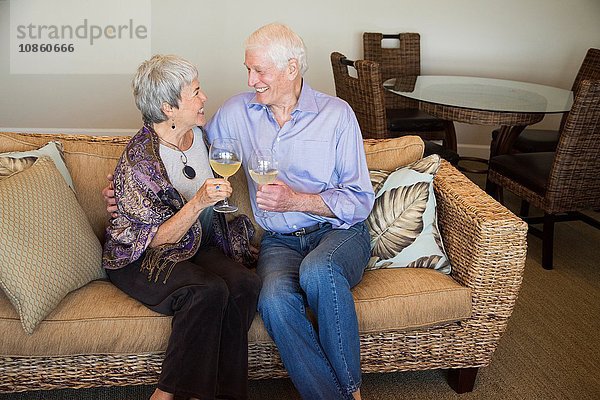 Älteres Ehepaar entspannt sich auf dem Sofa  hält ein Glas Wein in der Hand und lächelt
