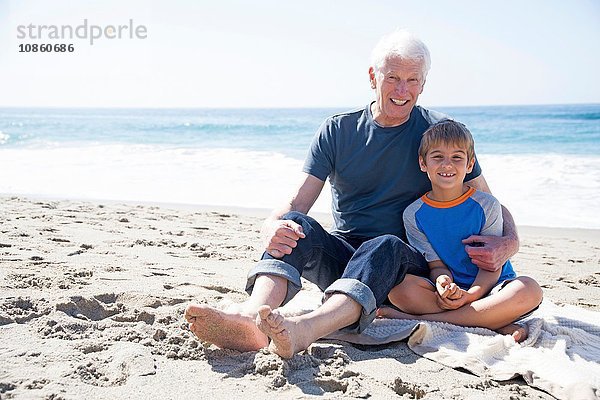 Porträt von Großvater und Enkel  am Strand sitzend  lächelnd