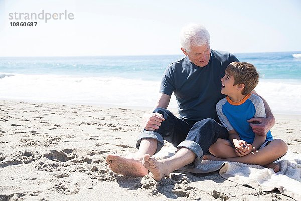 Großvater und Enkel sitzen am Strand und lächeln