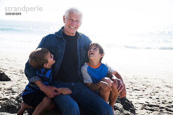 Großvater mit zwei Enkeln  am Strand sitzend  lächelnd