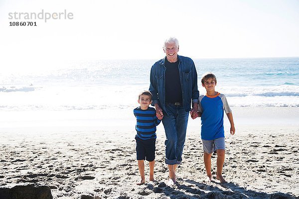 Großvater mit zwei Enkeln  am Strand spazieren  lächelnd
