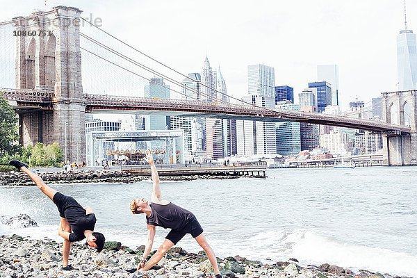 Zwei Männer beim Yoga am Flussufer vor der Brooklyn Bridge  New York  USA