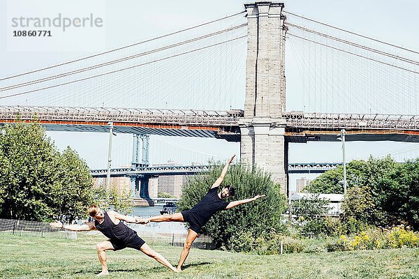 Zwei Männer  die sich im Yoga-Fuss seitwärts lehnen  halten Position vor der Brooklyn Bridge  New York  USA