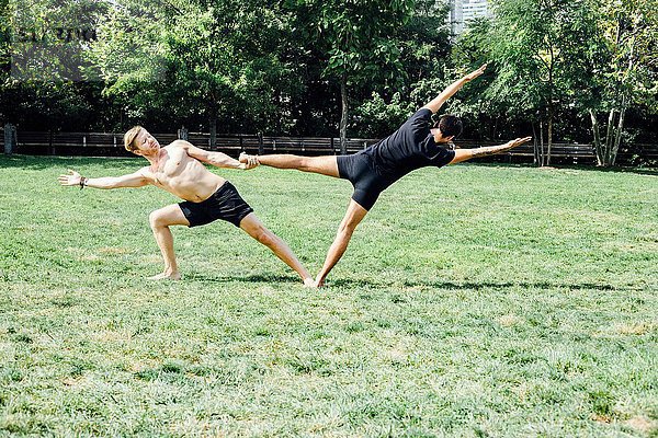 Zwei Männer  die Yoga-Fußübungen machen  halten Position im Park