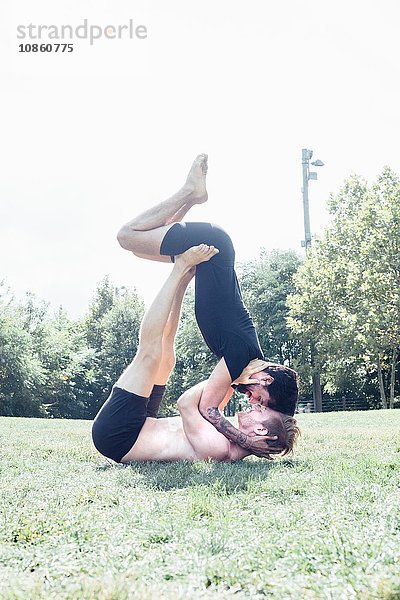 Zwei Männer stehen sich im Park in einer Yogastellung von Angesicht zu Angesicht gegenüber