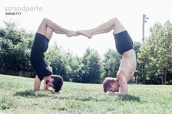 Zwei Männer in Yogastellung im Park auf dem Kopf stehend