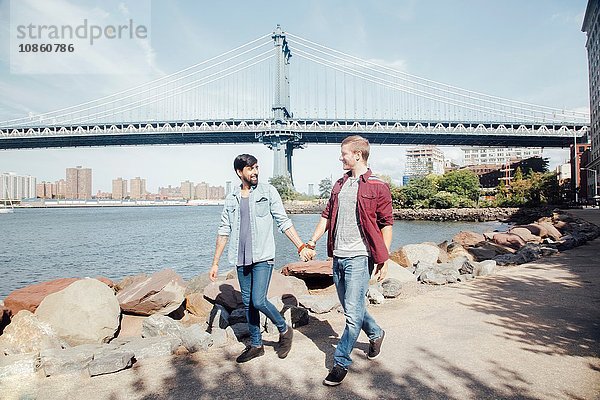 Männliches Paar beim Spaziergang am Flussufer bei der Manhattan Bridge  New York  USA