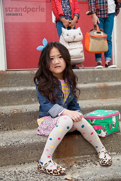 Porträt einer nervösen Grundschülerin  die auf der Treppe der Grundschule sitzt