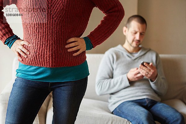 Schnappschuss einer Frau vor ihrem Freund auf dem Sofa beim Lesen eines Smartphones